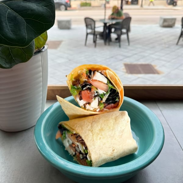 Two wraps filled with chicken, lettuce, tomatoes, and black beans in a teal bowl by a window.