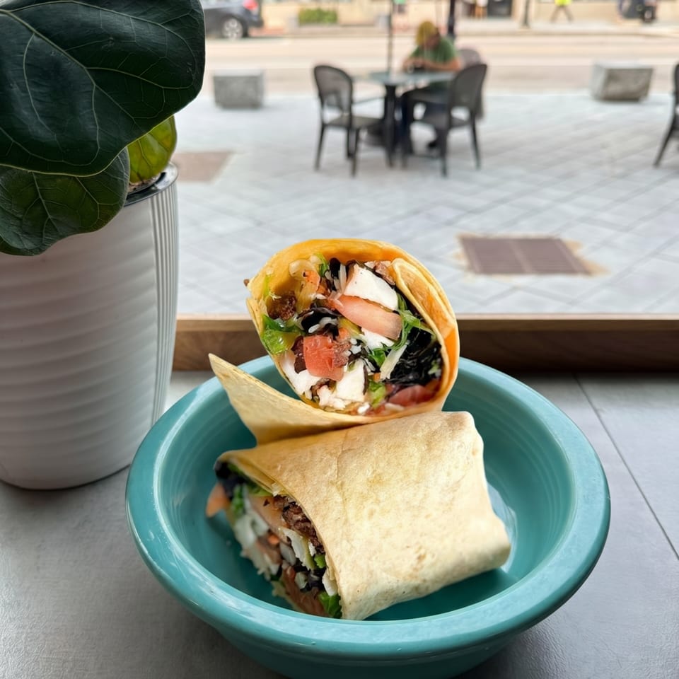 Two wraps filled with chicken, lettuce, tomatoes, and black beans in a teal bowl by a window.