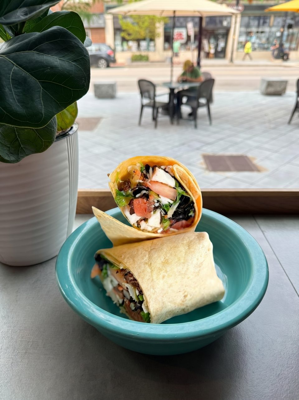 Two wraps filled with chicken, lettuce, tomatoes, and black beans in a teal bowl by a window.
