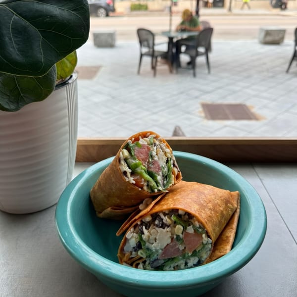 Two wraps filled with greens, cheese, and meat, served in a teal bowl by a window.