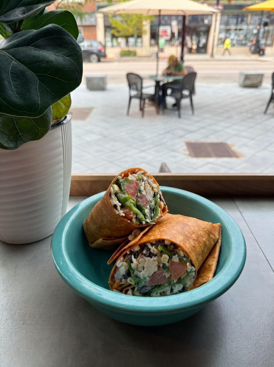 Two wraps filled with greens, cheese, and meat, served in a teal bowl by a window.