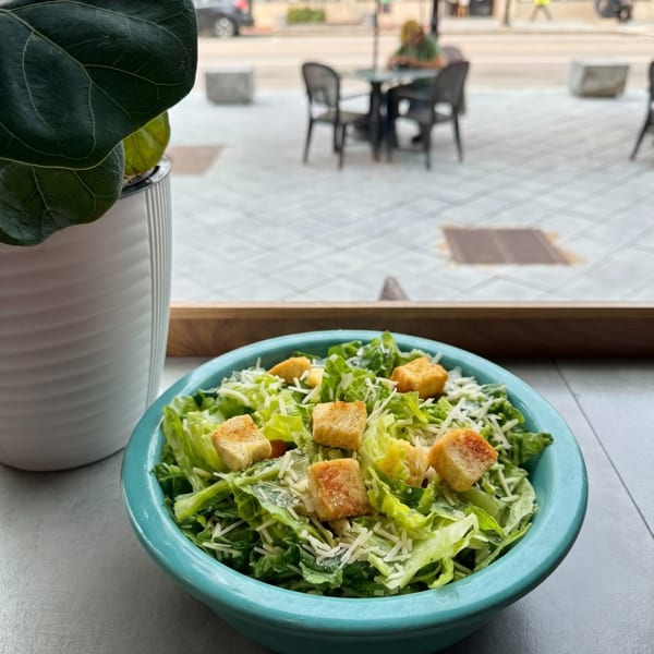 Caesar salad in a turquoise bowl with croutons and cheese, overlooking a street patio.
