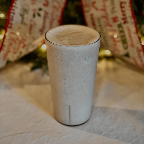 A tall glass of creamy white milkshake with foam on top, set against a festive Christmas background.
