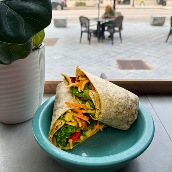 Two colorful wraps filled with vegetables in a teal bowl, with an outdoor street scene in the background.