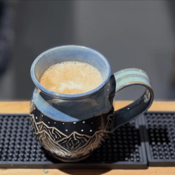 A blue and black ceramic mug with a mountain design, filled with a frothy coffee drink.